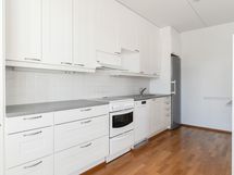 Valkoinen, siisti keittiö, jossa on hyvät säilytystilat ja työtasot.