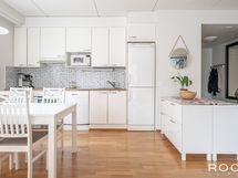 Moderni, vaaleasävyinen keittiö aputasoineen rajaa luontevan ruokailutilan ikkunan edustalle.