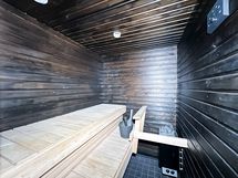 Tyylikäs tummaseinäinen sauna. Oman saunan löylyissä kelpaa rentoutua pitkän viikon päätteeksi.