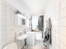 Siisti, osittain laatoitettu kylpyhuone jossa pyykinpesukone.